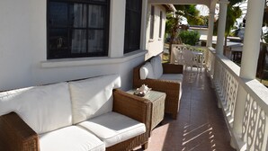 A covered outdoor seating area with wicker furniture and white cushions, a tiled floor, and a white railing with decorative cutouts. - Eullen Villa (Arthurs Seat)