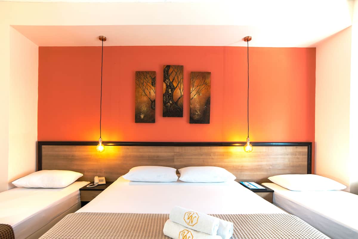 Quarto de hotel com uma cama grande, duas mesas de cabeceira, um telefone e uma parede com três quadros.