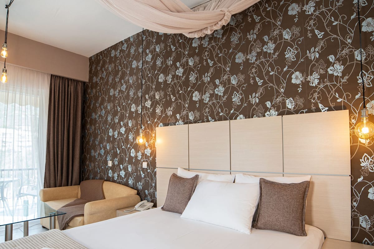 Quarto de hotel com uma cama grande, mesa de cabeceira, uma cadeira e uma janela com cortinas.