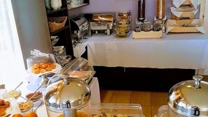 Montaje de bufé con diferentes platillos y bebidas, incluyendo frutas, ensaladas y bebidas calientes.