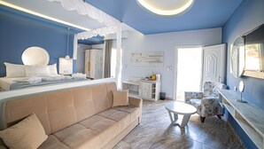 Habitación de hotel moderna con una cama grande, un sofá, una pequeña mesa redonda y una silla. Se ve un baño por una puerta abierta.