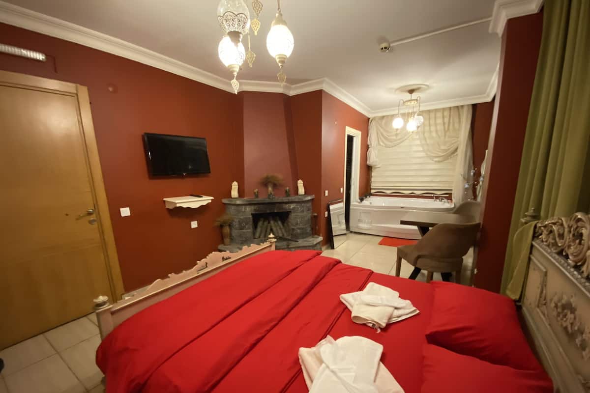 A bedroom with a large bed, a fireplace, a television, and a bathroom visible through an open door.
