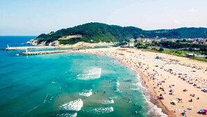 Una playa costera con aguas turquesas cristalinas, una orilla arenosa y colinas verdes al fondo.