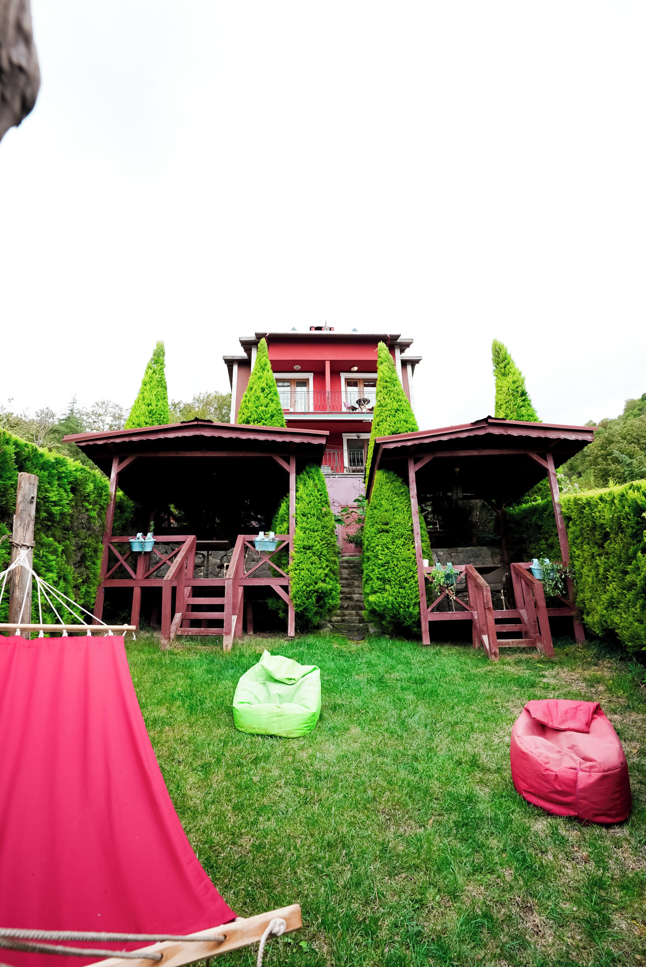 A red building with two wooden gazebos in front, a red tent, and a green bean bag chair on a grassy lawn.