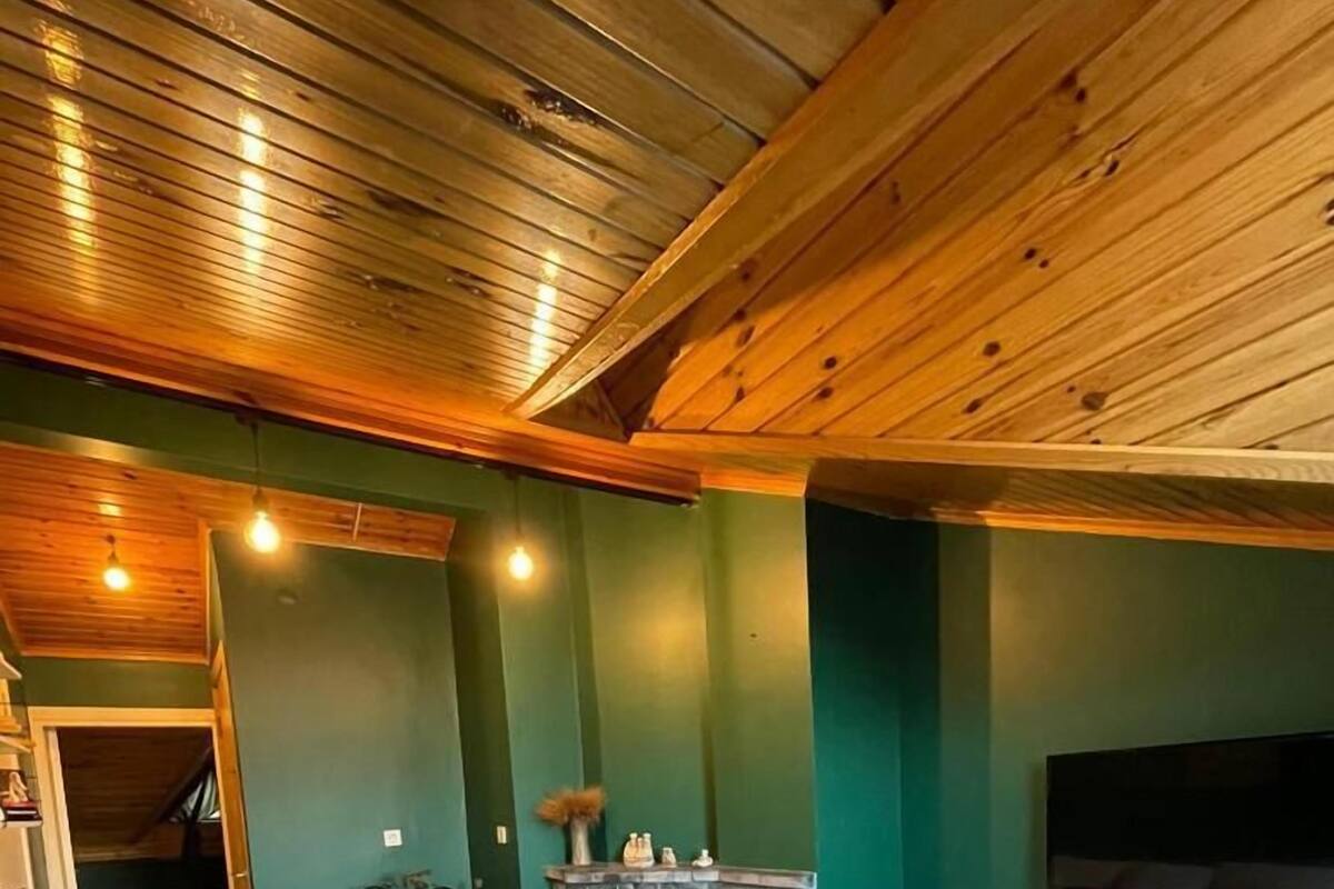 A cozy living room with a stone fireplace, a sofa with cushions, a television mounted on the wall, and a wooden ceiling.