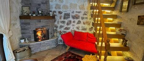 A cozy interior with a stone wall, a fireplace, a wooden staircase, and a red sofa.