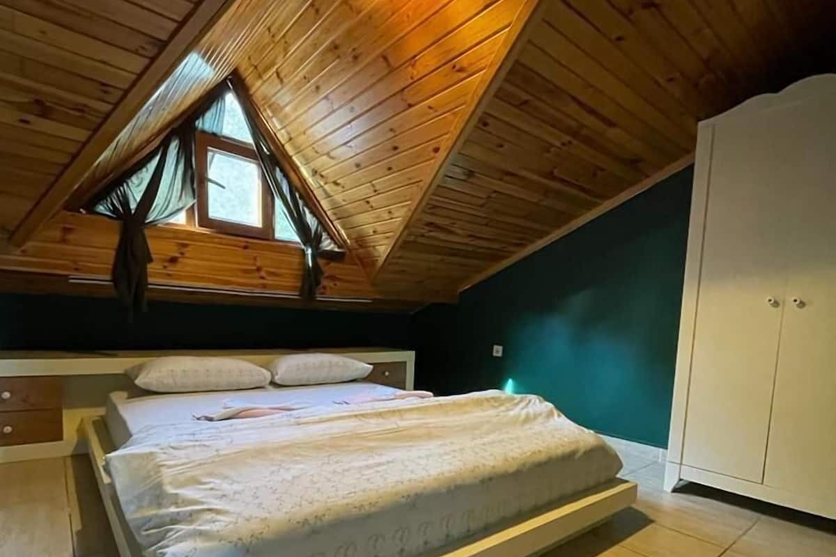 A bedroom with a sloped ceiling, a bed, a wardrobe, and a window.
