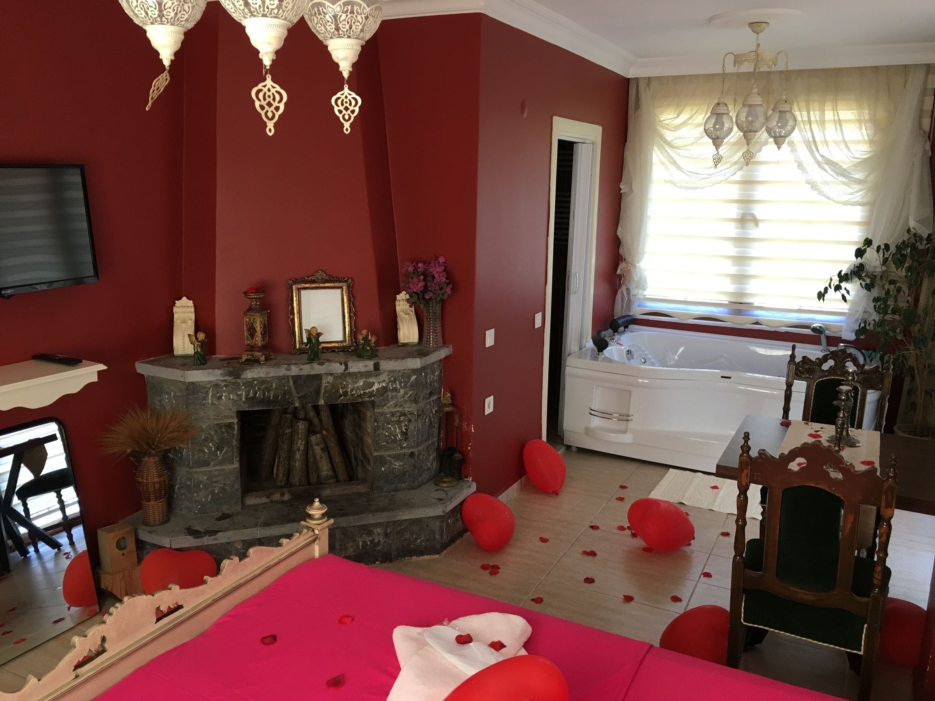 Una habitación con chimenea de piedra, una cama con pétalos de rosa, una bañera y un televisor en la pared.