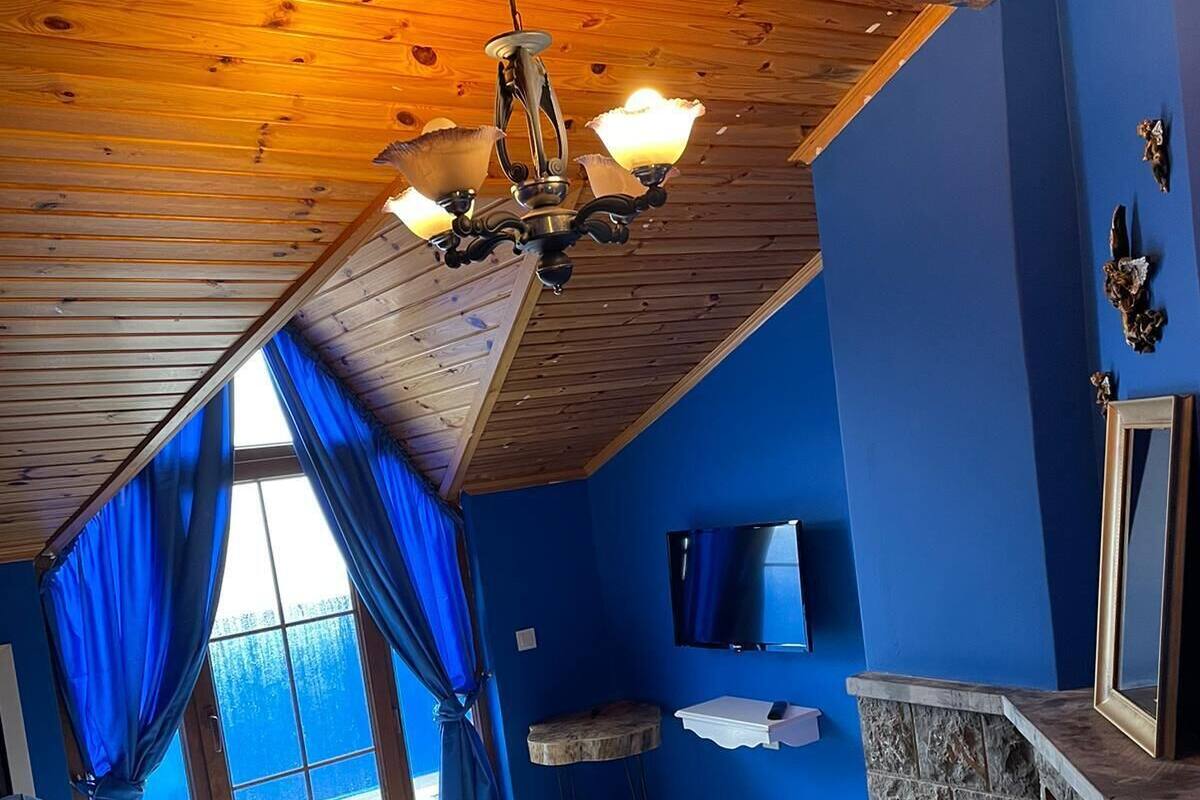 A cozy living room with a wooden ceiling, blue walls, a stone fireplace, a sofa, and a TV.