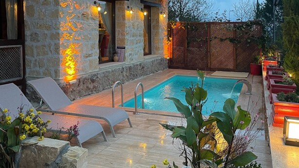Un edificio de piedra con piscina, mobiliario exterior y terraza de madera.