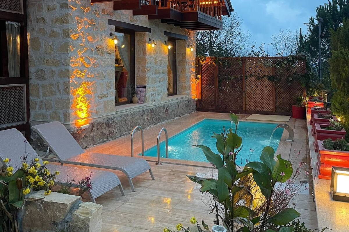 A stone building with a pool, outdoor seating, and a wooden deck.
