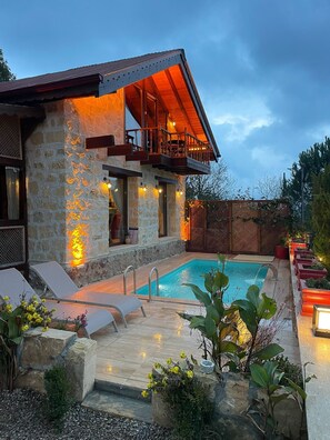 Un edificio de piedra con piscina, mobiliario exterior y terraza de madera.
