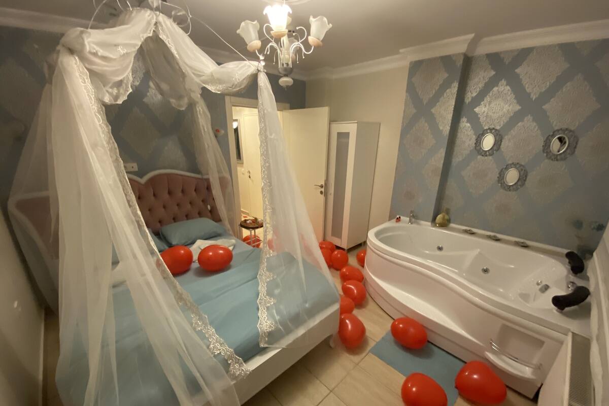 A bedroom with a canopy bed, a large bathtub, and red balloons scattered on the floor.