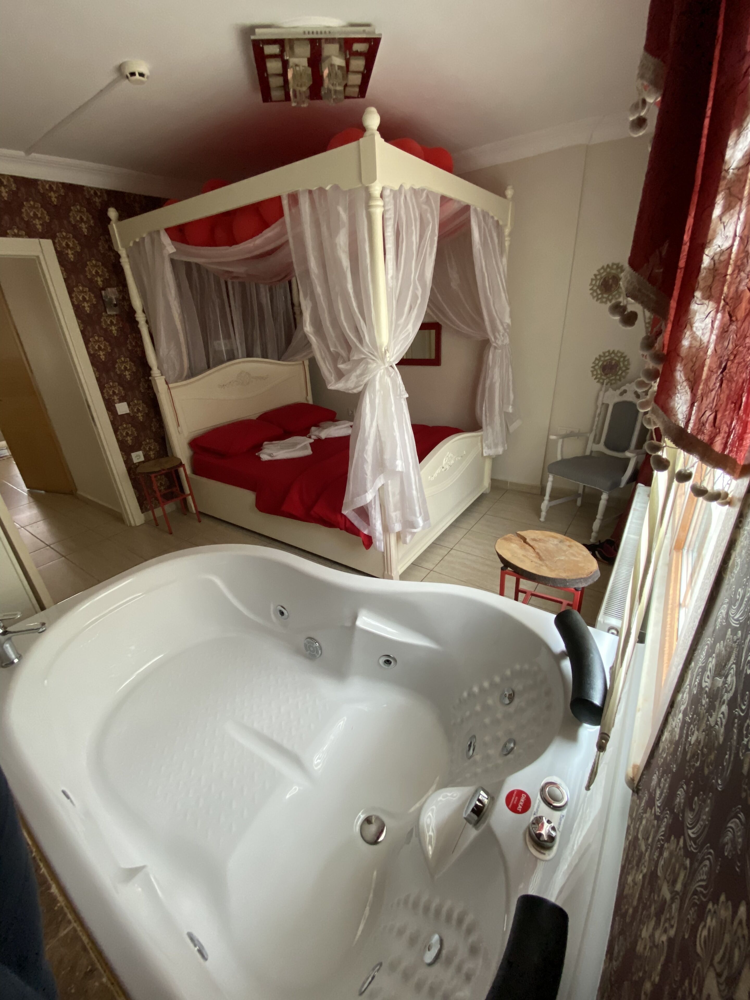 A bedroom with a four-poster bed, a large bathtub, a small table, and a chair.