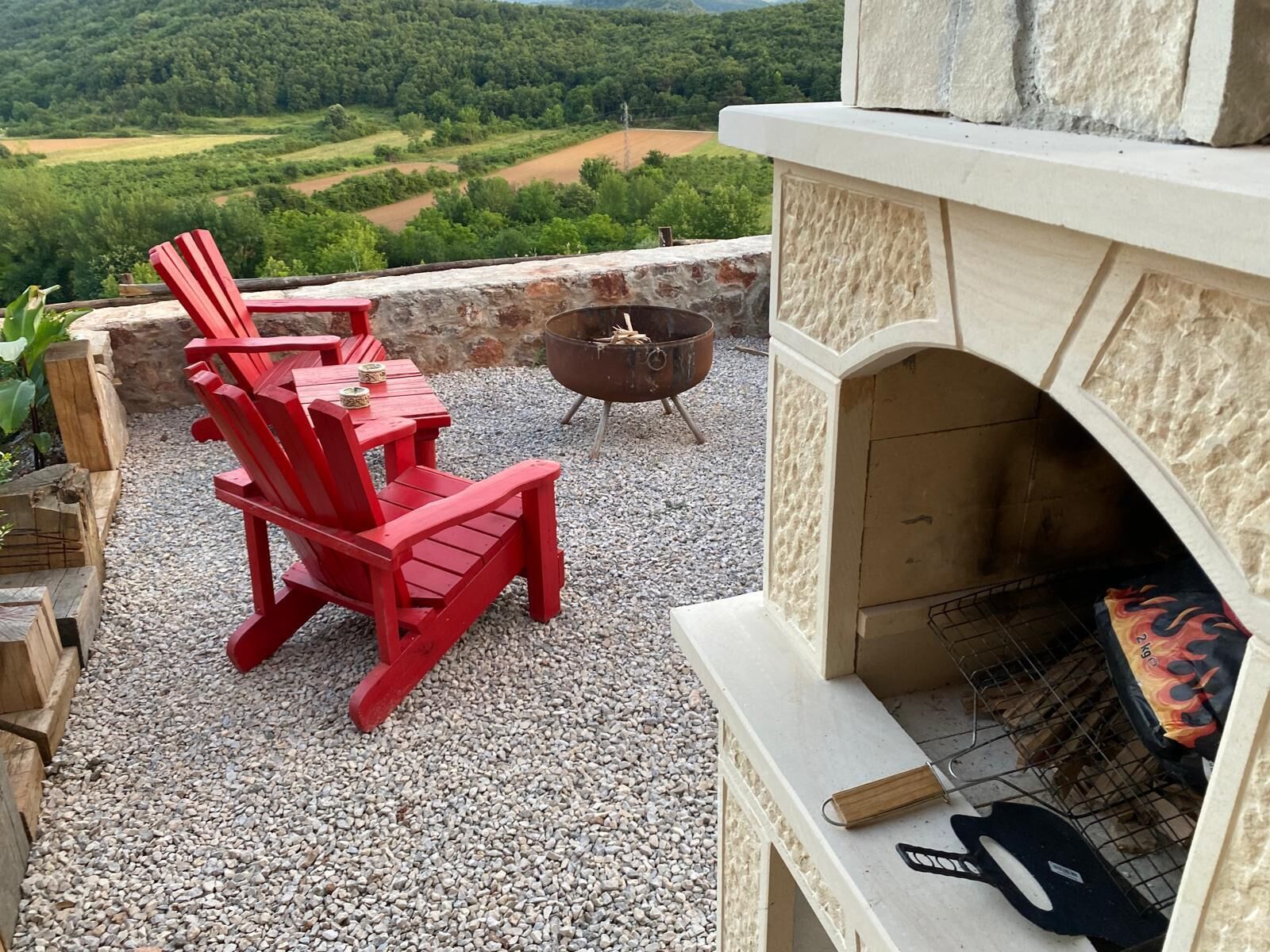 Un patio al aire libre con sillas Adirondack rojas, una chimenea de piedra y una fogata.