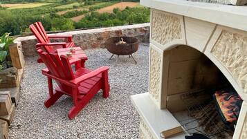 Un patio al aire libre con sillas Adirondack rojas, una chimenea de piedra y una fogata.