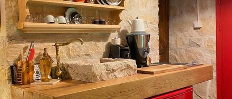 A kitchen with wooden shelves holding dishes and glasses, a coffee machine, and a red cabinet.
