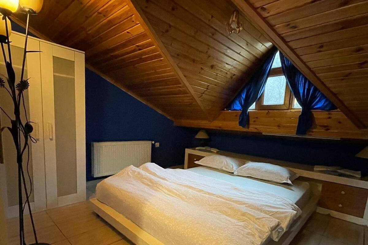 A bedroom with a sloped ceiling, a bed, a radiator, and a window with curtains.