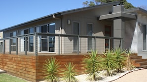 A modern two-story house with a wooden deck and a small garden with agave plants. - Malbecs (Lake Tyers Beach)
