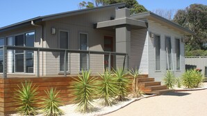 A modern two-story house with a flat roof, large windows, and a wooden deck. - Malbecs (Lake Tyers Beach)