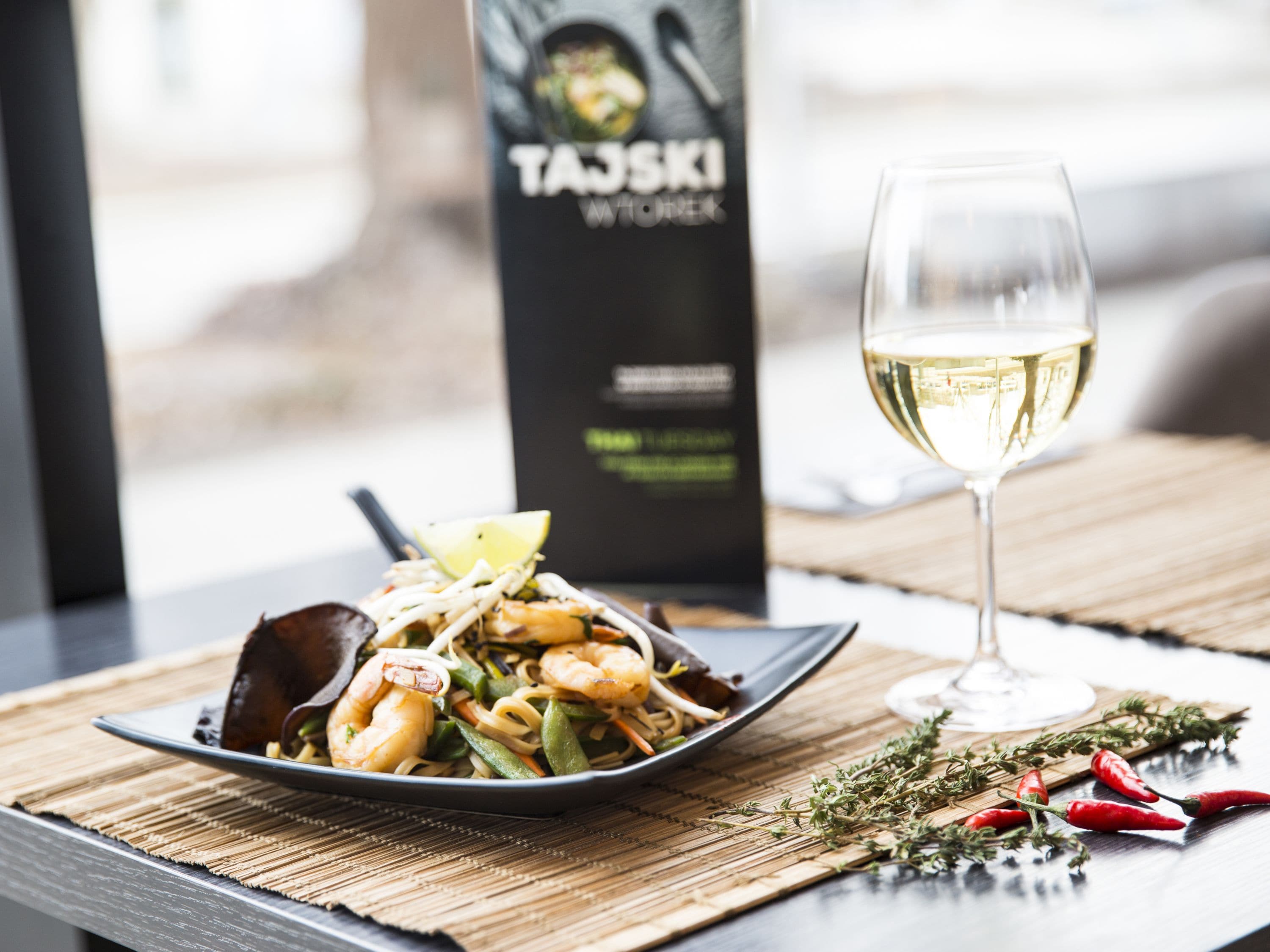 A plate of seafood pasta with a glass of white wine on a table with a menu in the background.