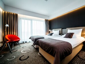 A modern hotel room with a large bed, a red chair, and a large window with curtains. - Q Hotel Plus Krakow (Kraków)