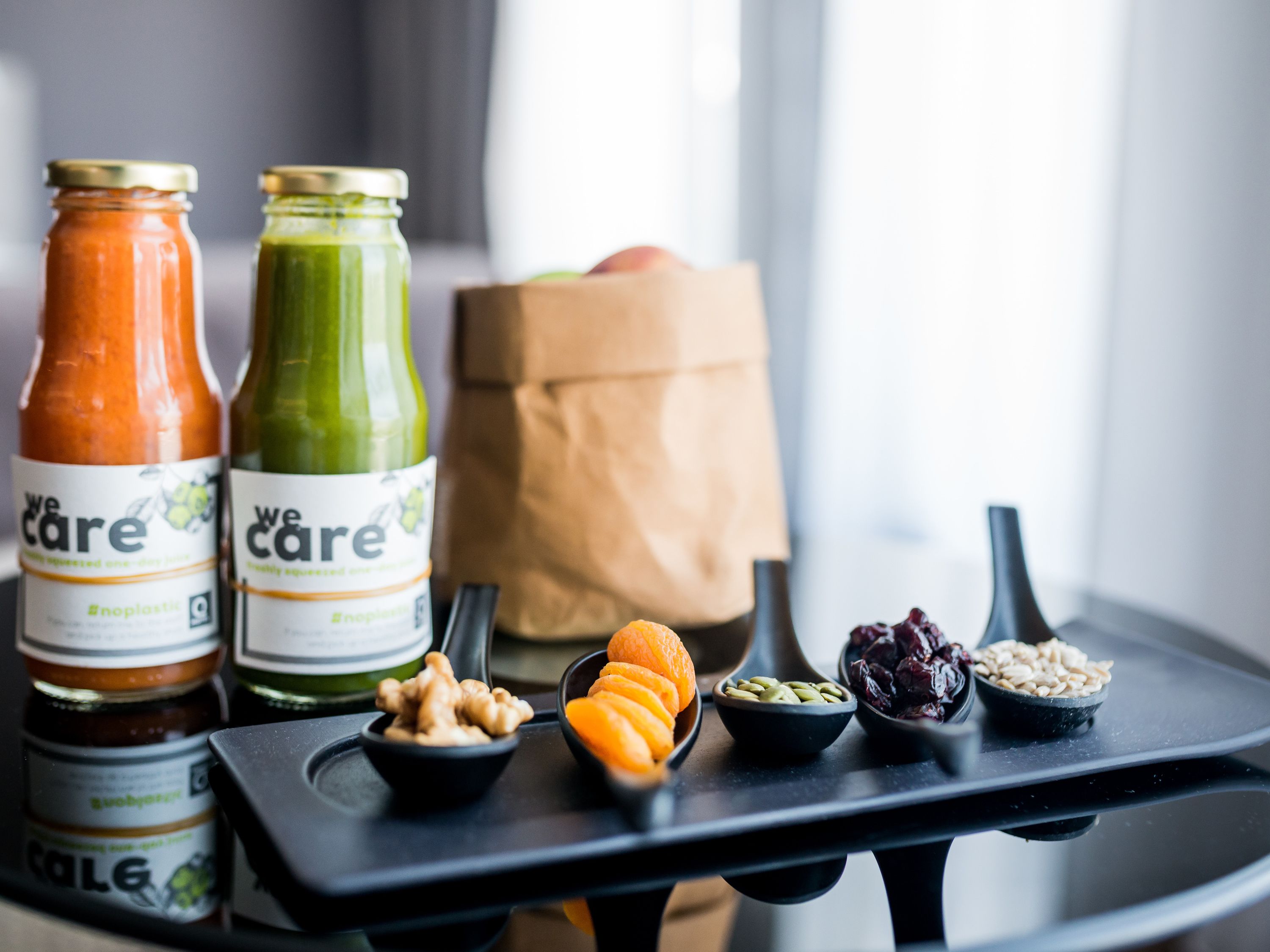 A tray with two bottles of juice, a paper bag, and bowls of nuts and dried fruits.