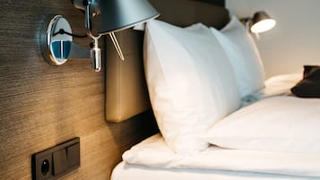 Un lit bien fait, avec du linge de lit blanc, une lampe fixée au mur et un panneau de commande sur la tête de lit.