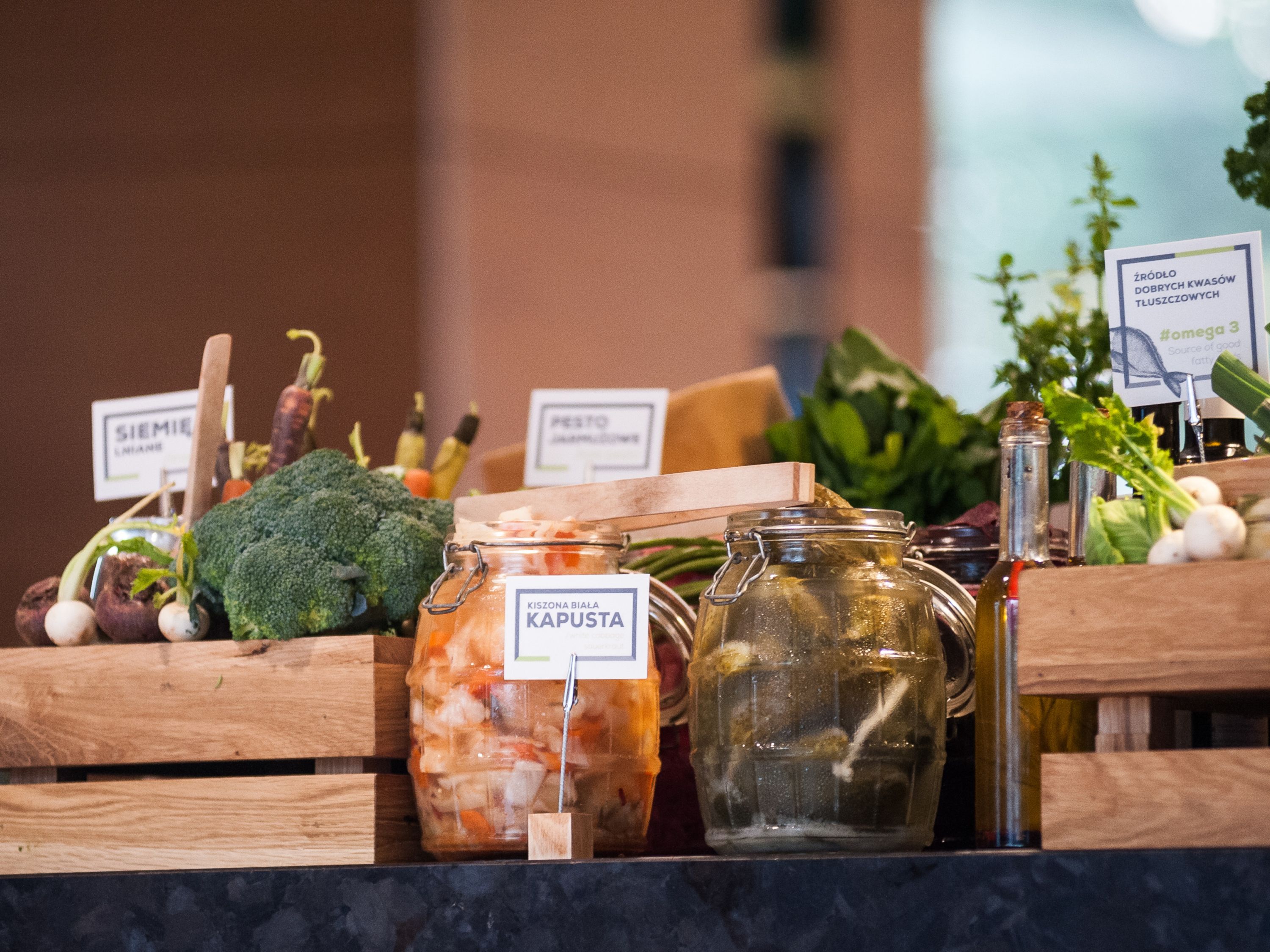 Exhibición de vegetales y hierbas en conserva en cajas de madera, con etiquetas que indican nombres y tipos.