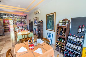 A restaurant with multiple tables, chairs, and a wine rack with various bottles. - Villas Playa Hermosa Beach Hotel (Sardinal)