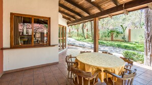 Eine überdachte Terrasse mit einem runden Tisch, Holzstühlen, einem Deckenventilator und Blick auf einen Garten.