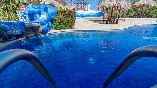 Ein Swimmingpool mit klarem, blauem Wasser, umgeben von tropischer Vegetation und Reetdachschirmen.