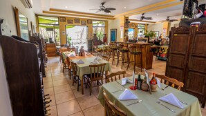 Ein Restaurant mit mehreren Tischen, Stühlen, Deckenventilatoren und einer Bar.