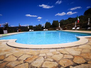 A swimming pool with stone tiles, surrounded by lounge chairs and umbrellas. - Locanda Vesuna (Trequanda)