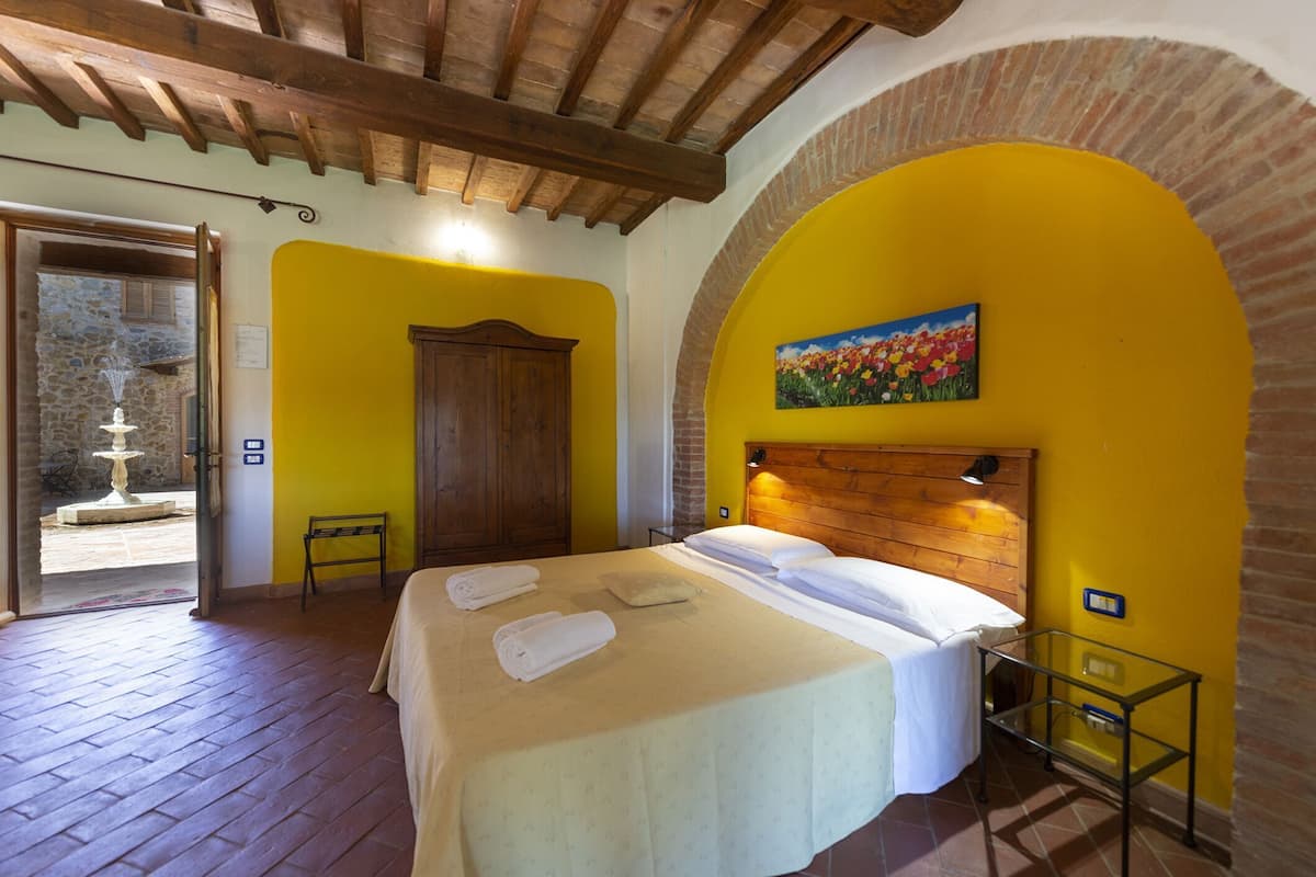 A room with a bed, a wooden headboard, a painting, and a door leading to an outdoor area.