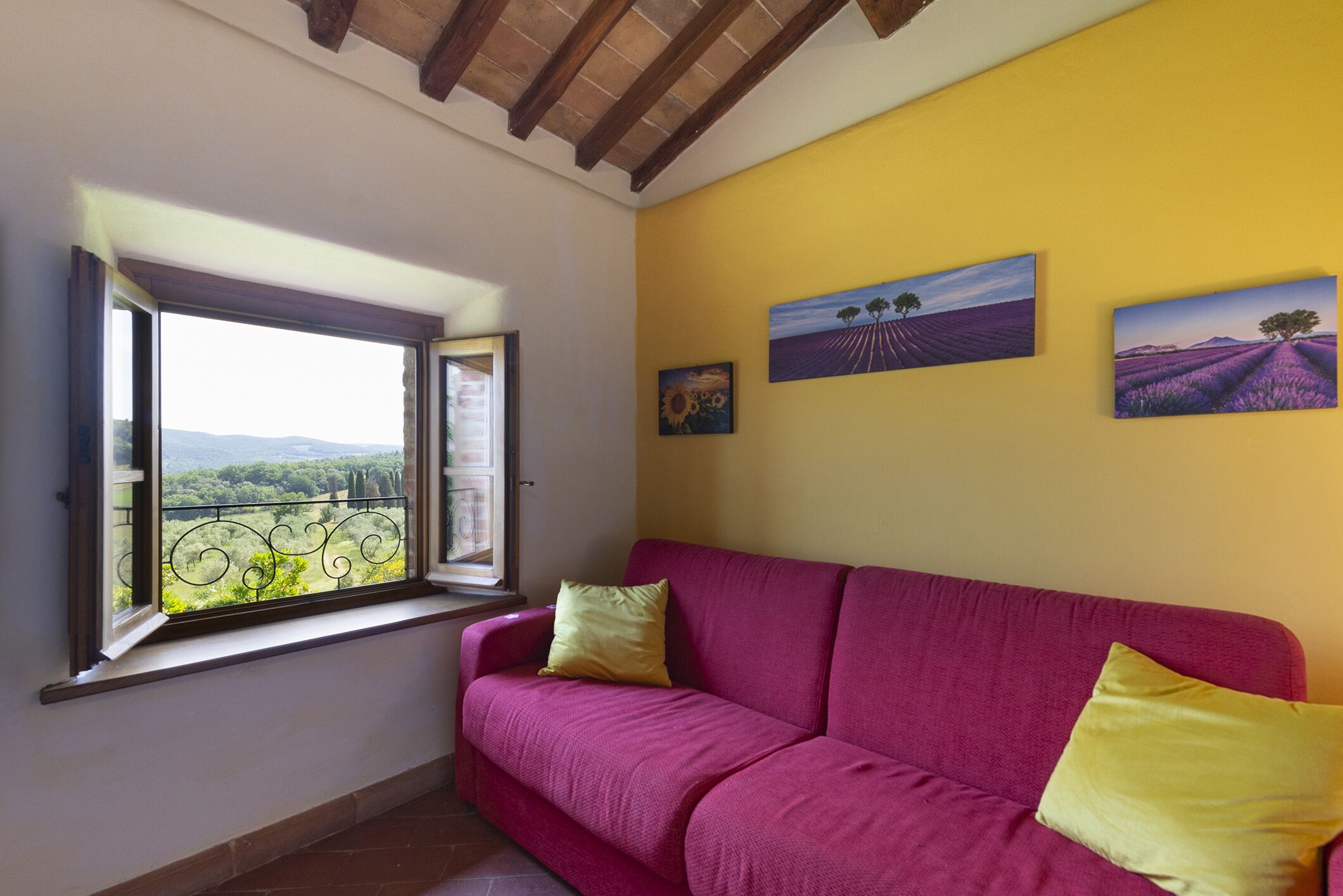 A room with a pink sofa, a window with a view of greenery, and two landscape paintings on the wall.