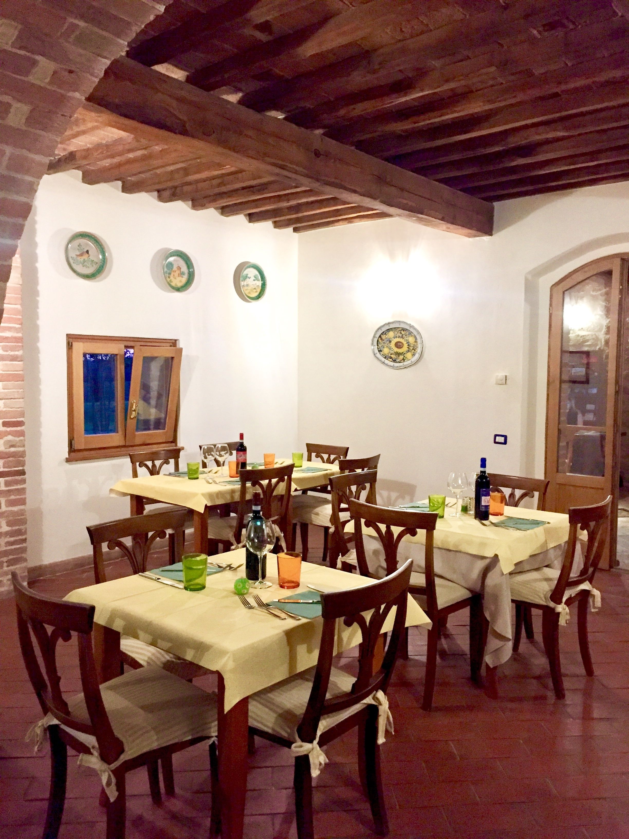 A dining area with wooden tables and chairs, a brick wall, and a wooden ceiling.