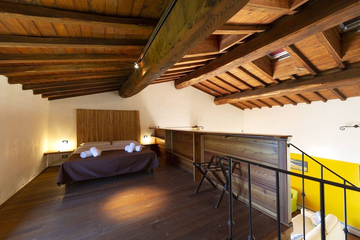A bedroom with a wooden ceiling, a bed with a brown bedspread, a nightstand, and a chair.