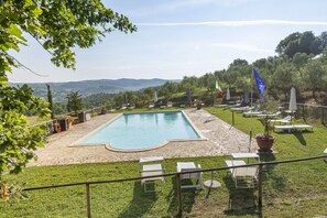 A swimming pool with lounge chairs and umbrellas, surrounded by a stone deck and a grassy area with trees. - Locanda Vesuna (Trequanda)