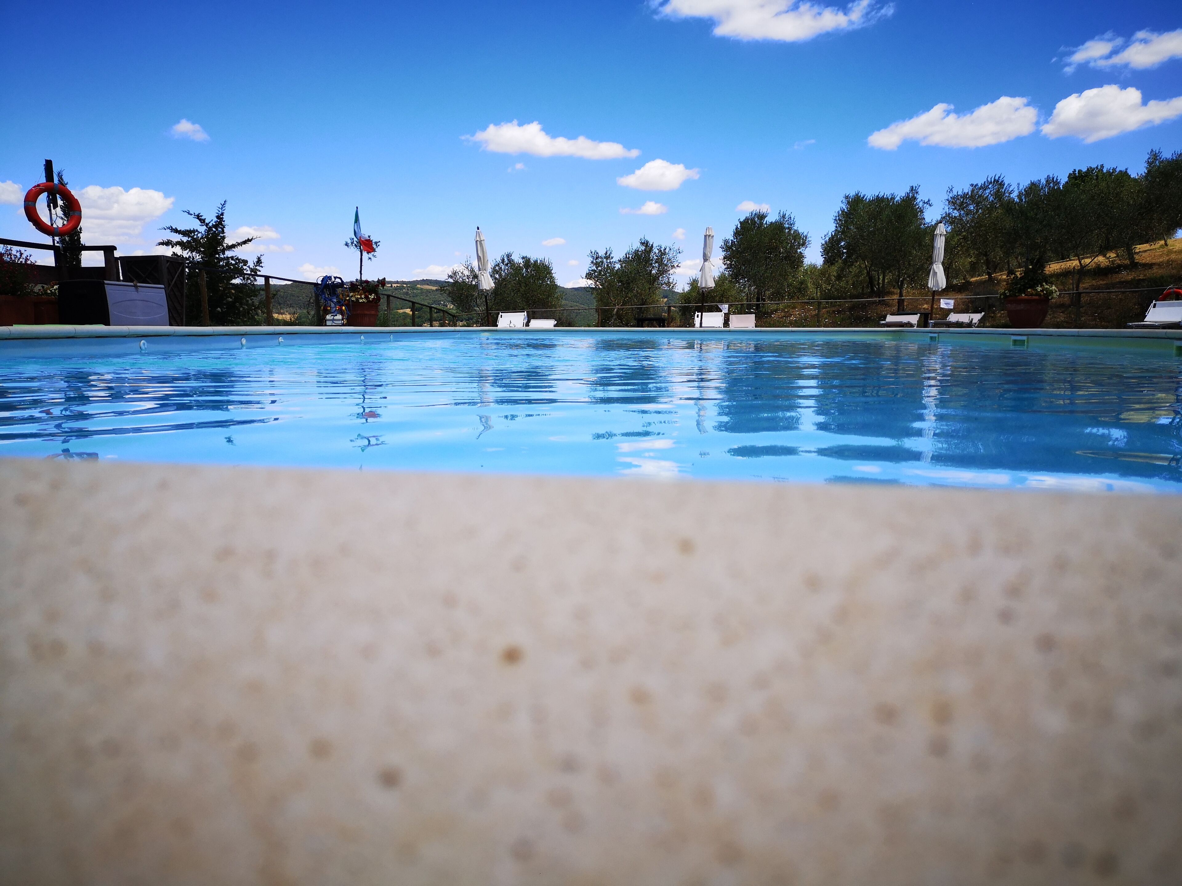 Ein Schwimmbecken mit klarem, blauem Wasser, umgeben von Bäumen und Flaggen.