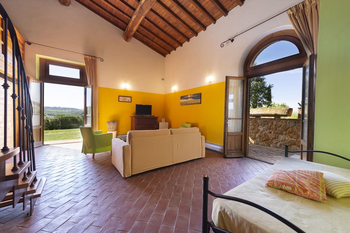 A spacious room with a wooden ceiling, a sofa, a bed, and a view of the outdoors.