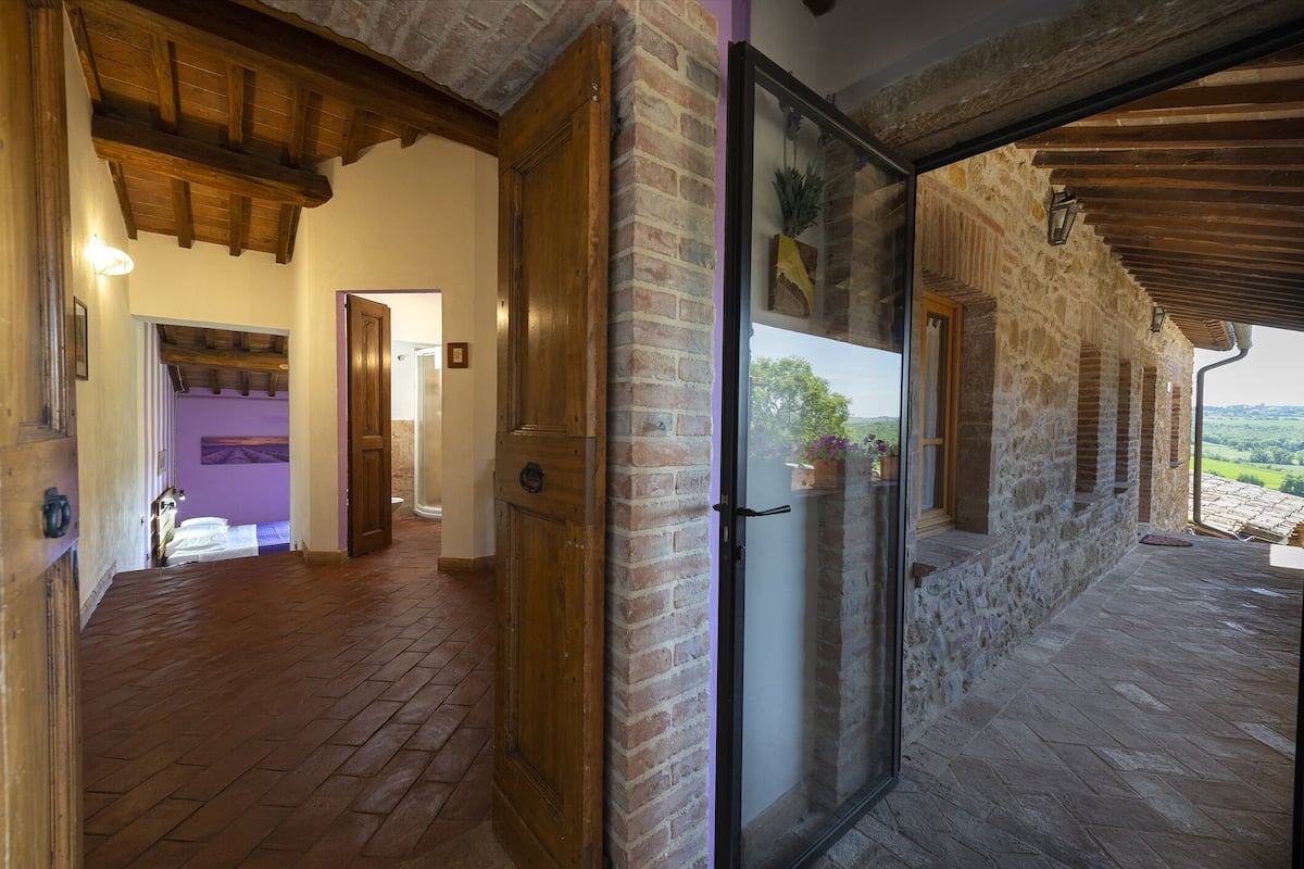 A rustic interior with a wooden floor, stone walls, and a glass door leading to an outdoor area with a view of the countryside.