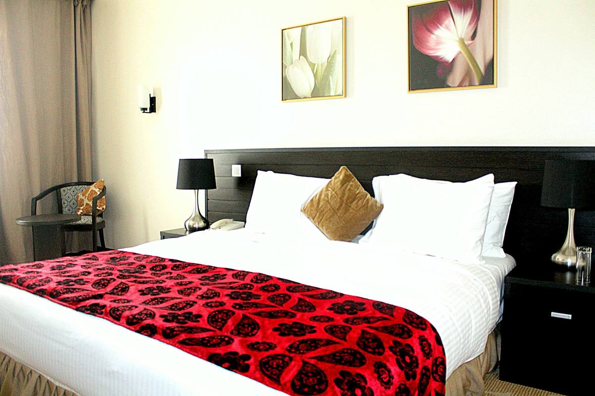 A hotel room with a bed, a nightstand, a lamp, and two wall-mounted pictures.