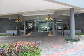 Una entrada de hotel moderna con suelo de baldosas, dos candelabros y una puerta de cristal que da a la recepción.