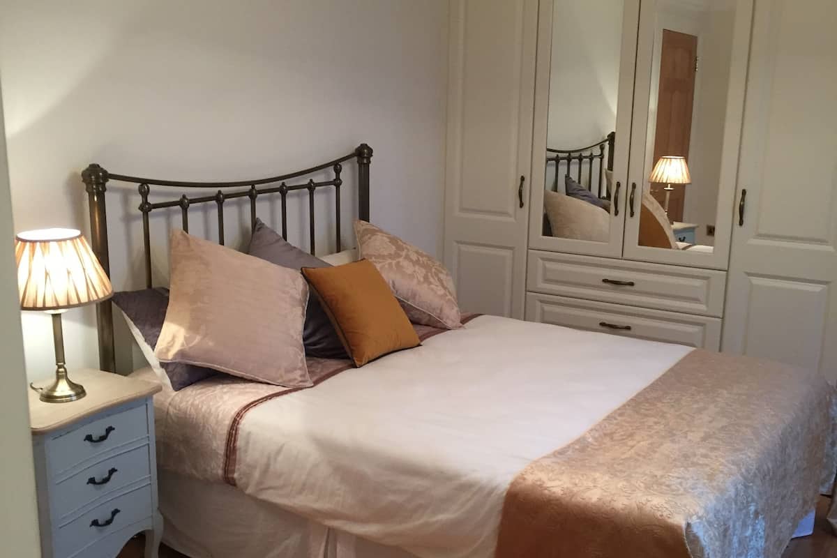 A neatly made bed with a headboard, a bedside lamp, and a dresser with drawers.