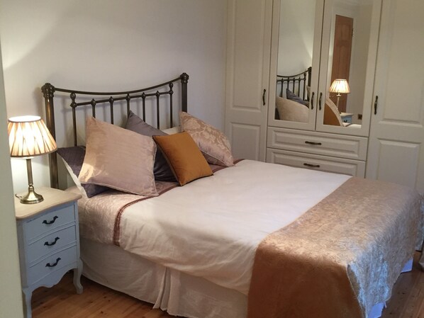 Una cama bien hecha con cabecera, lámpara de noche y cómoda con cajones.
