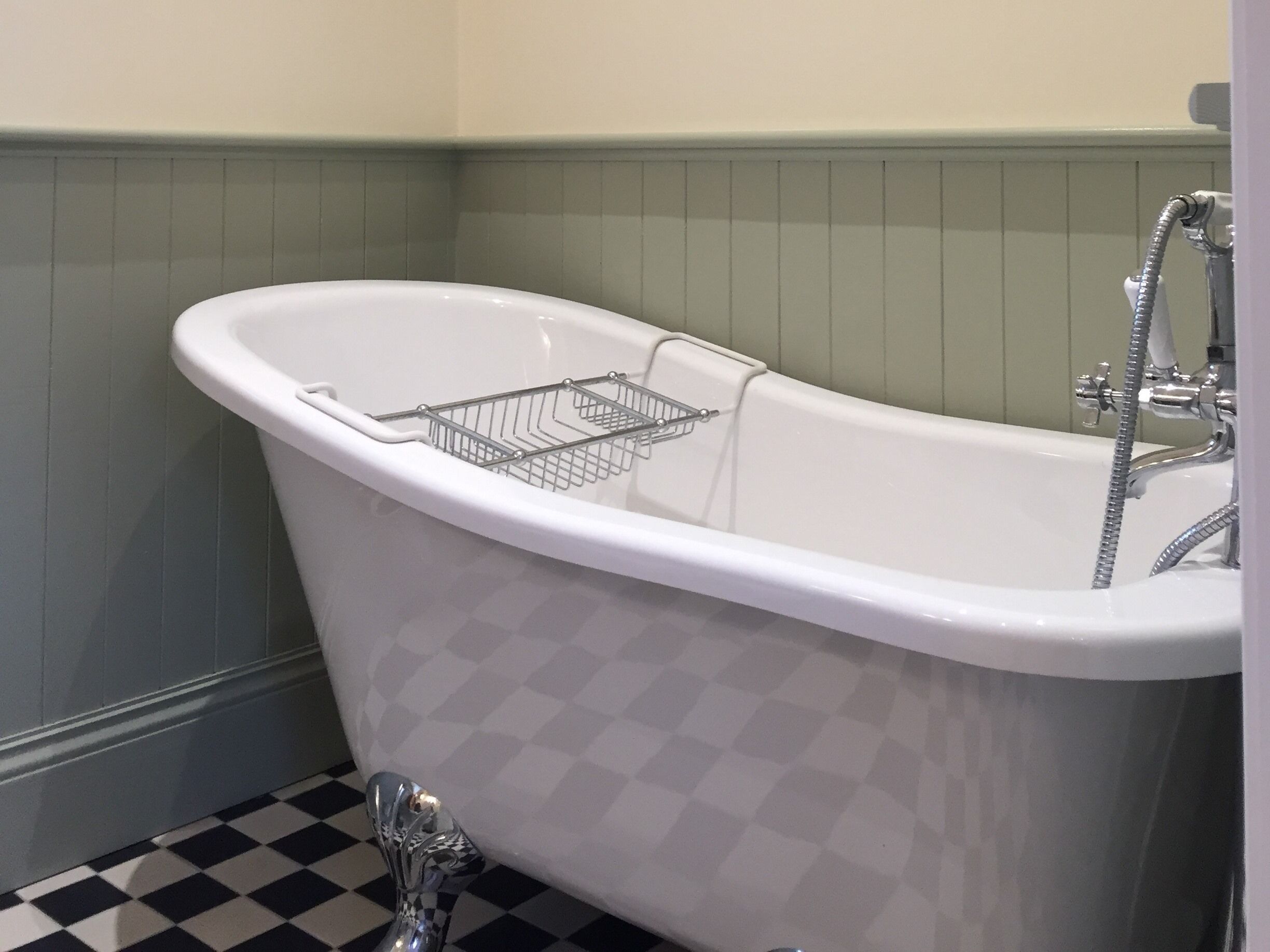 A white freestanding bathtub with a chrome faucet and a chrome showerhead, a chrome shower hose, and a chrome shower head.