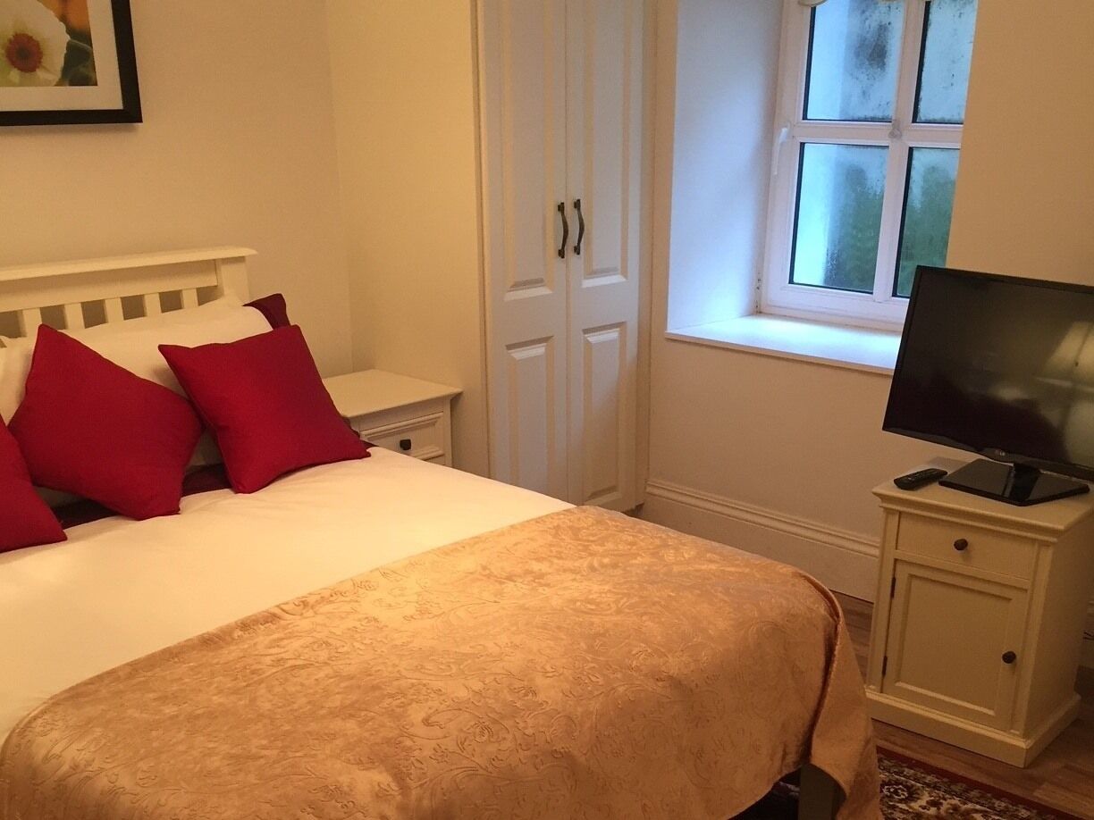 Un dormitorio con cama, televisor sobre una mesita de noche, ventana con vistas y una puerta.