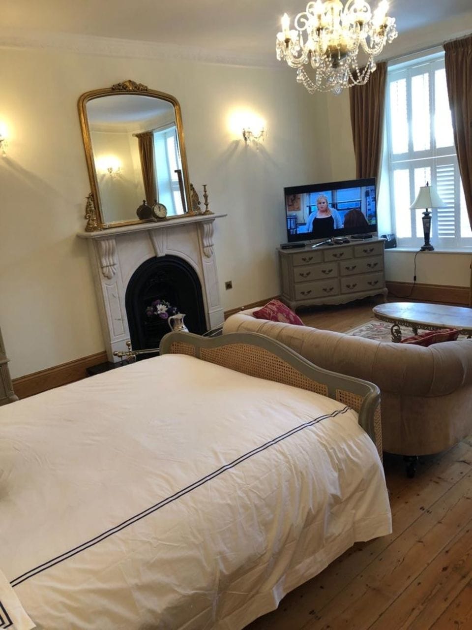 A bedroom with a large bed, a television, a fireplace, and a chandelier.