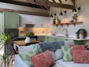 A cozy kitchen with green cabinets, a wooden dining table, and a sofa with patterned cushions. - Pardlestone Farm – Self-Catering Cottages (Bridgwater)